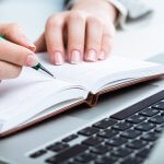 ノートPCの前でノートにメモを取る手元